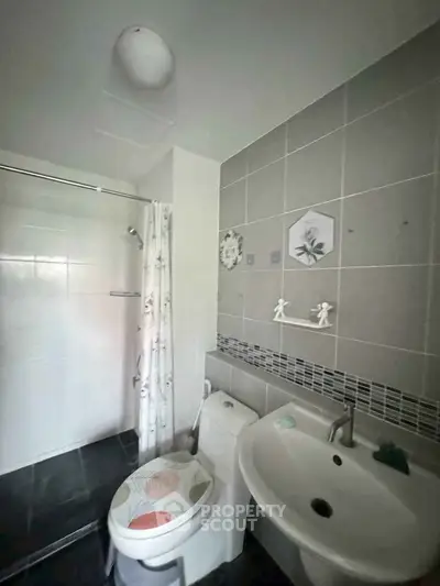 Modern bathroom with sleek tiles and shower area, featuring a stylish sink and toilet.