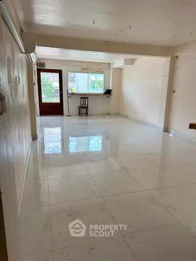 Spacious empty living room with glossy white tile flooring and large windows for natural light.