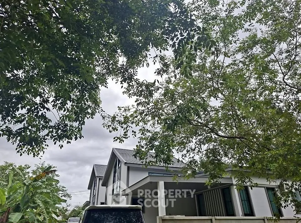 Modern two-story house with lush greenery and overcast sky, perfect for serene living.