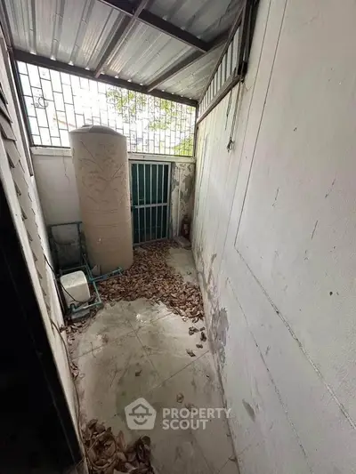 Compact outdoor storage area with metal roof and water tank, ideal for utility use.