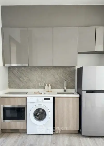 Modern kitchen with sleek cabinets, washing machine, and stainless steel fridge in compact layout.