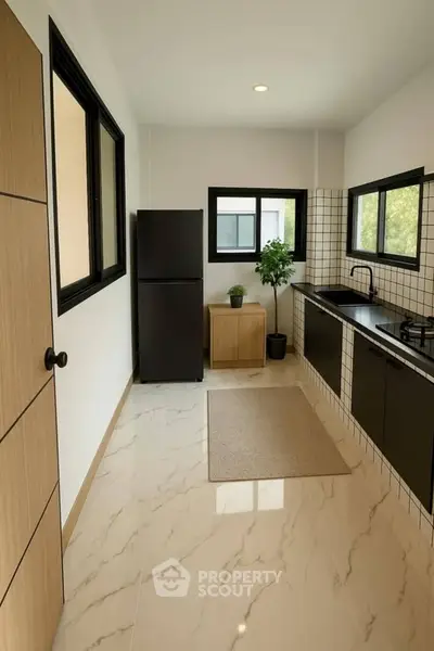 Modern kitchen with sleek black cabinets, gas stove, and large fridge in a bright, tiled space.