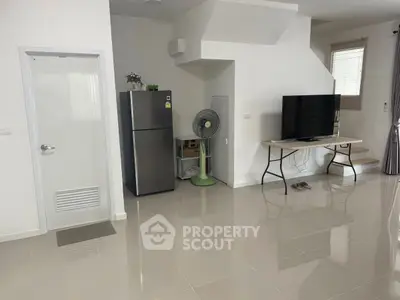 Spacious modern living room with sleek tiled flooring, featuring a large TV and refrigerator, ideal for contemporary living.