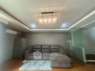 Modern living room with stylish gray sofa and elegant lighting, featuring a sleek glass partition and air conditioning.