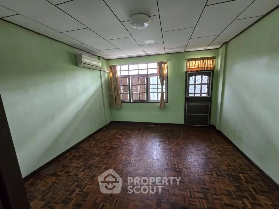 Spacious empty room with parquet flooring and large window in a residential property.