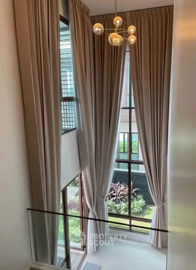 Elegant high-ceiling living room with large windows and modern chandelier.