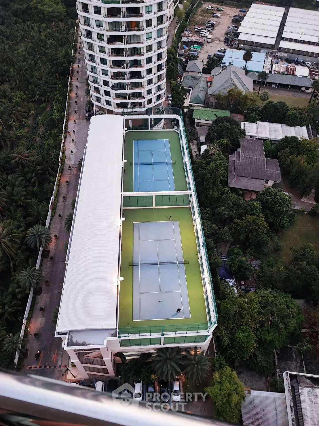 Aerial view of modern building with rooftop tennis courts and lush surroundings.