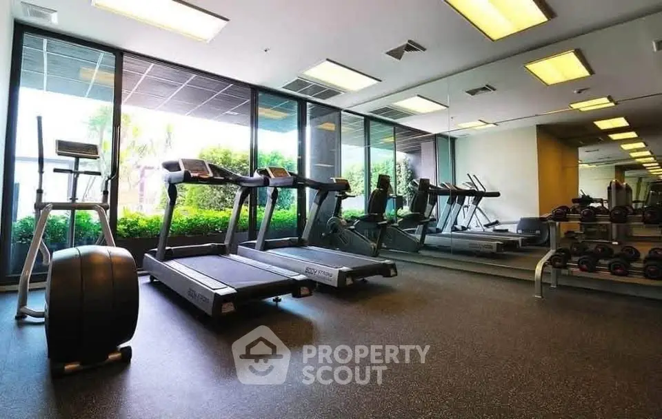 Modern gym with treadmills and weights in a bright, spacious setting with large windows.