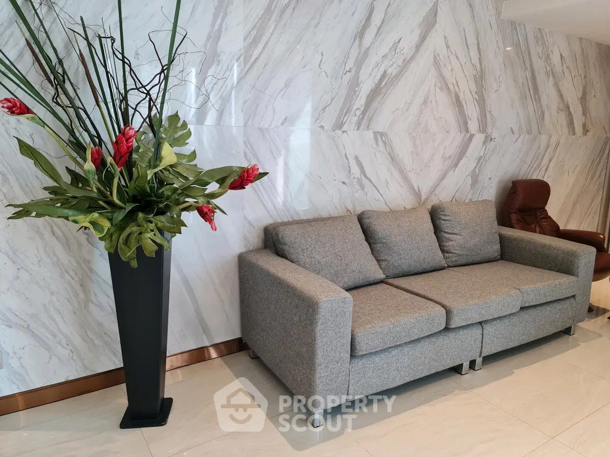 Elegant lobby with modern gray sofa and stylish floral arrangement, featuring marble walls and sleek flooring.
