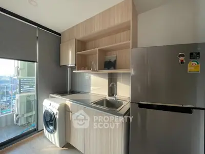 Modern kitchen with washing machine and fridge, featuring sleek cabinetry and natural light.