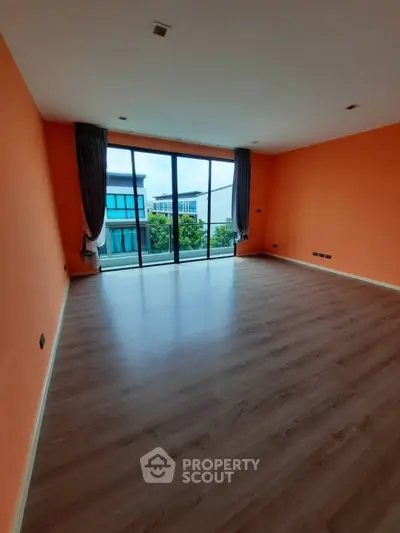 Spacious empty room with large windows and vibrant orange walls, offering a modern and bright living space.
