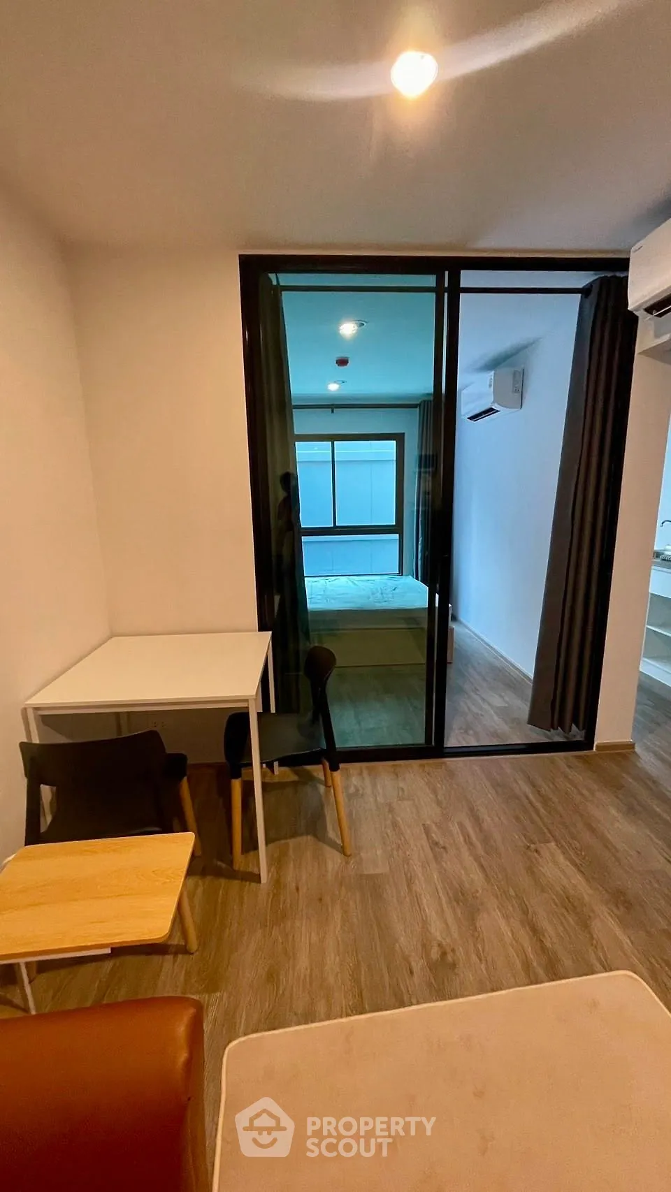 Modern apartment interior with open layout and bedroom view, featuring sleek furniture and wood flooring.