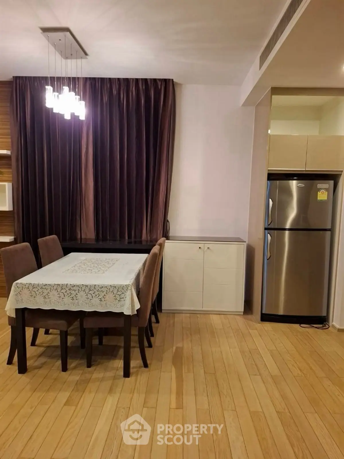 Elegant dining area with modern lighting and stainless steel fridge in stylish apartment.