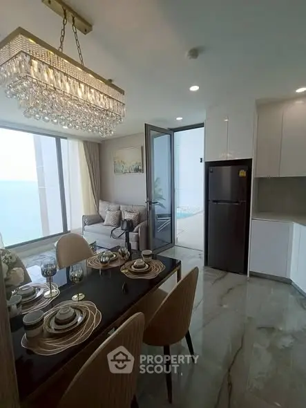Luxurious dining and living area with ocean view, elegant chandelier, and modern furnishings.