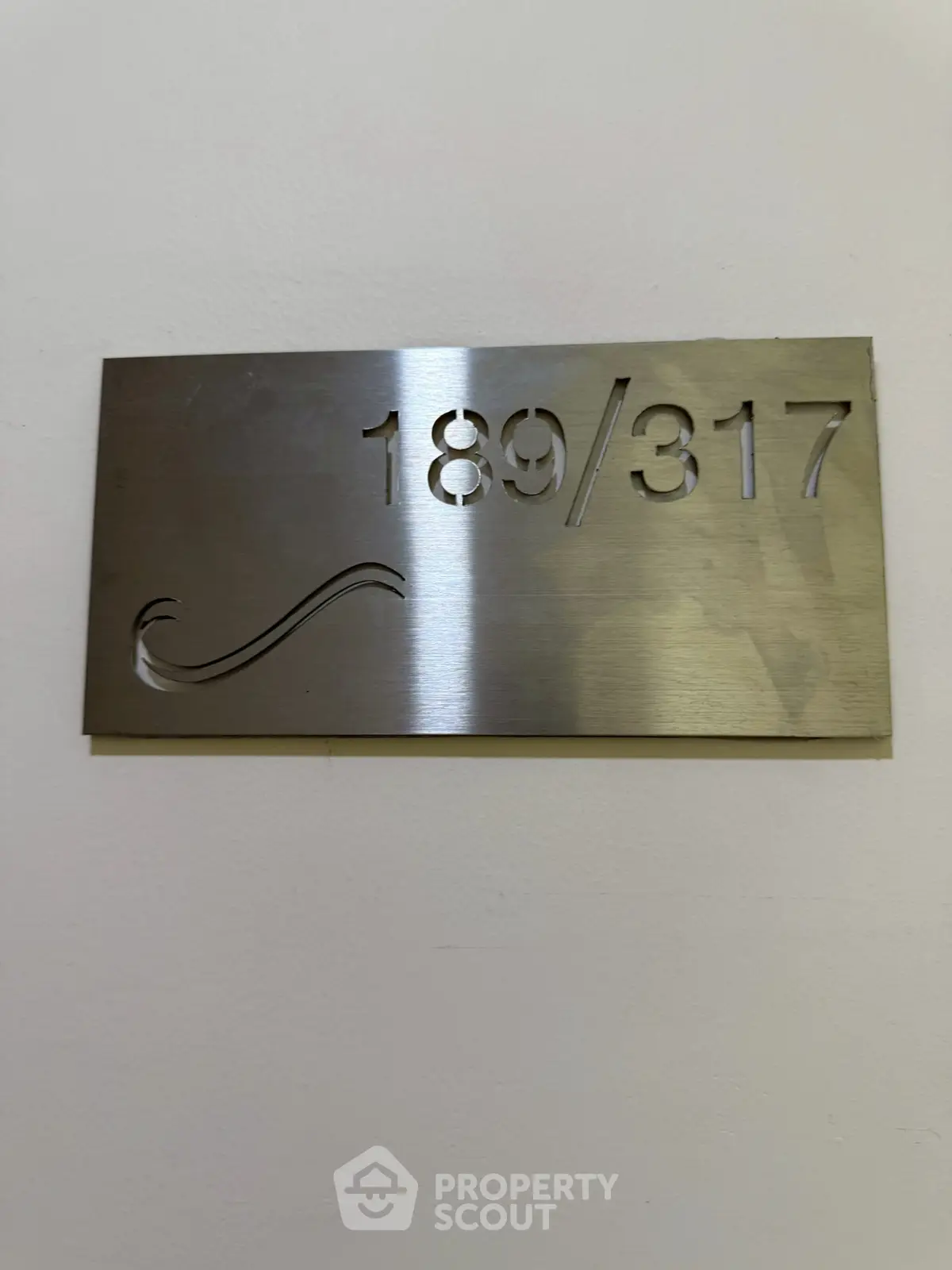 Stylish metallic apartment number plaque on a white wall