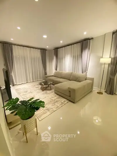 Elegant living room with modern decor and large windows, featuring a cozy sectional sofa and stylish lighting.