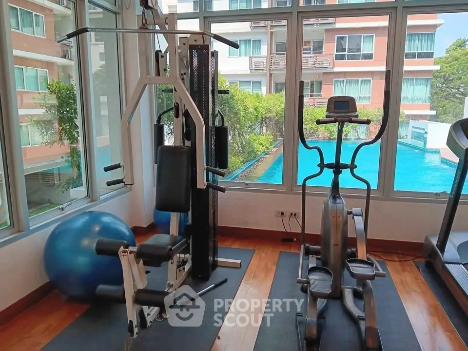 Modern gym with exercise equipment and pool view in luxury apartment complex.