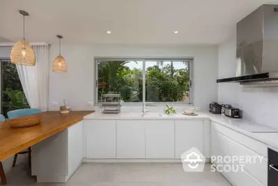 Modern kitchen with white cabinets, large window, and wooden breakfast bar in tropical setting.