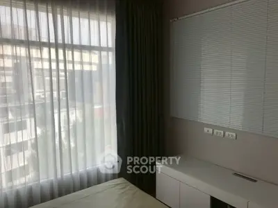 Modern bedroom with large window and sleek blinds, offering natural light and urban views.