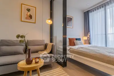 Modern studio apartment with stylish decor, featuring a cozy living area and a comfortable bed separated by glass partition.