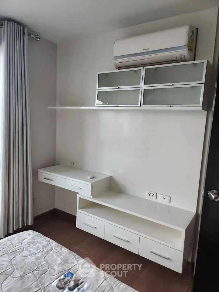 Modern bedroom with built-in storage and air conditioning unit, featuring sleek white furniture and natural light.