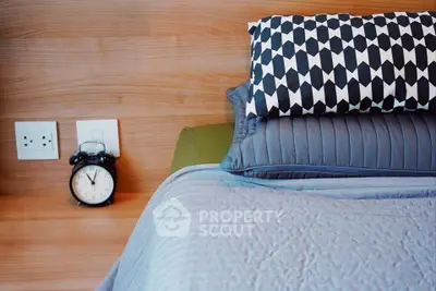 Cozy bedroom corner with stylish bedding and classic alarm clock on wooden nightstand.