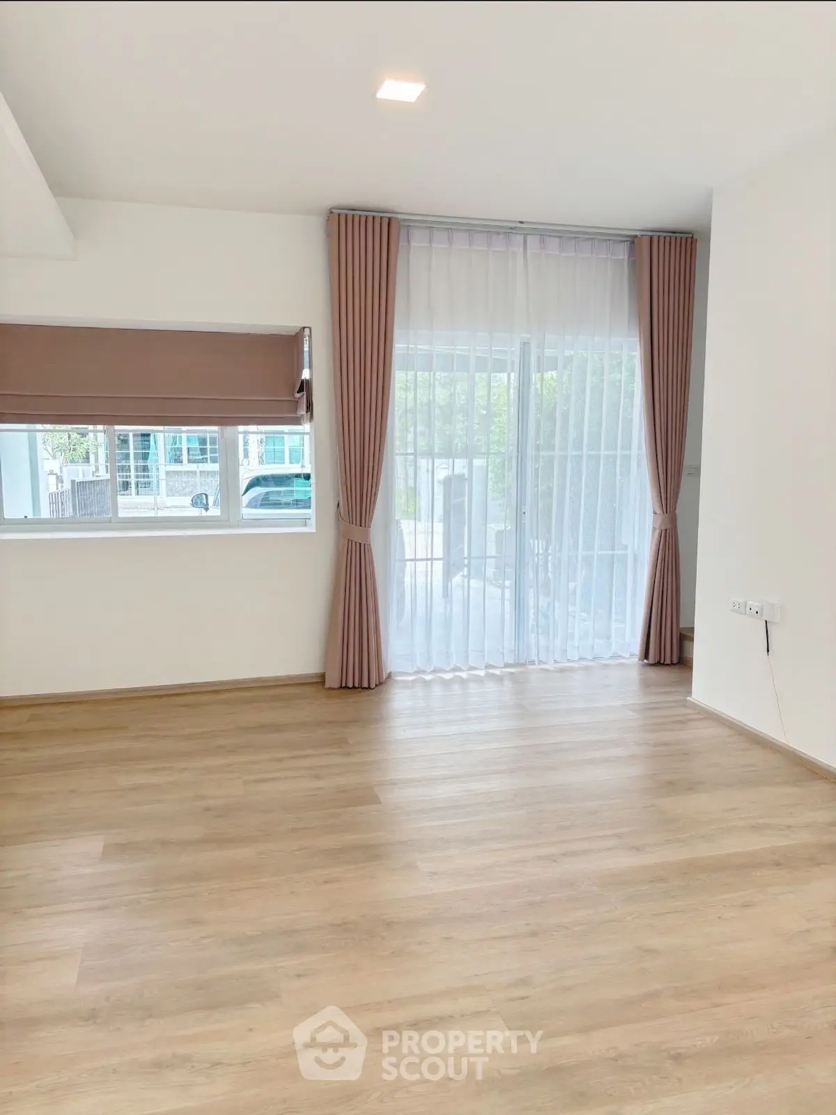 Spacious living room with large windows and elegant curtains, featuring light wood flooring.