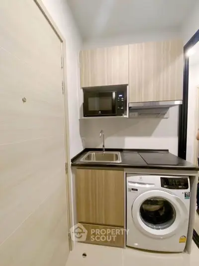 Compact kitchen with washing machine and modern cabinetry in a cozy apartment.