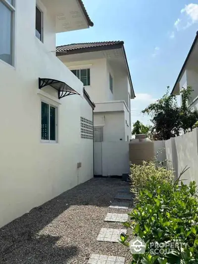 Charming two-story house with side garden and pathway under clear blue sky.