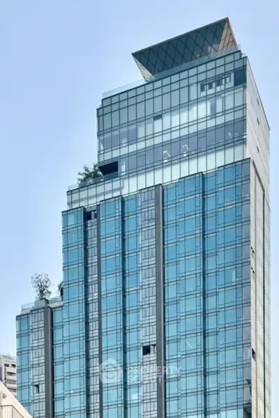 Modern glass skyscraper with unique rooftop design and lush greenery accents.