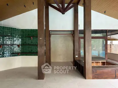 Spacious open-plan interior with high ceilings and rustic wooden beams, featuring green tiled accent wall.