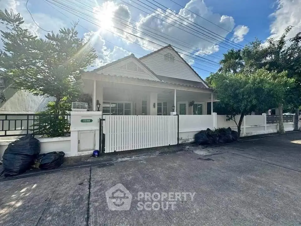 Charming single-story house with white picket fence and lush greenery under a bright blue sky.