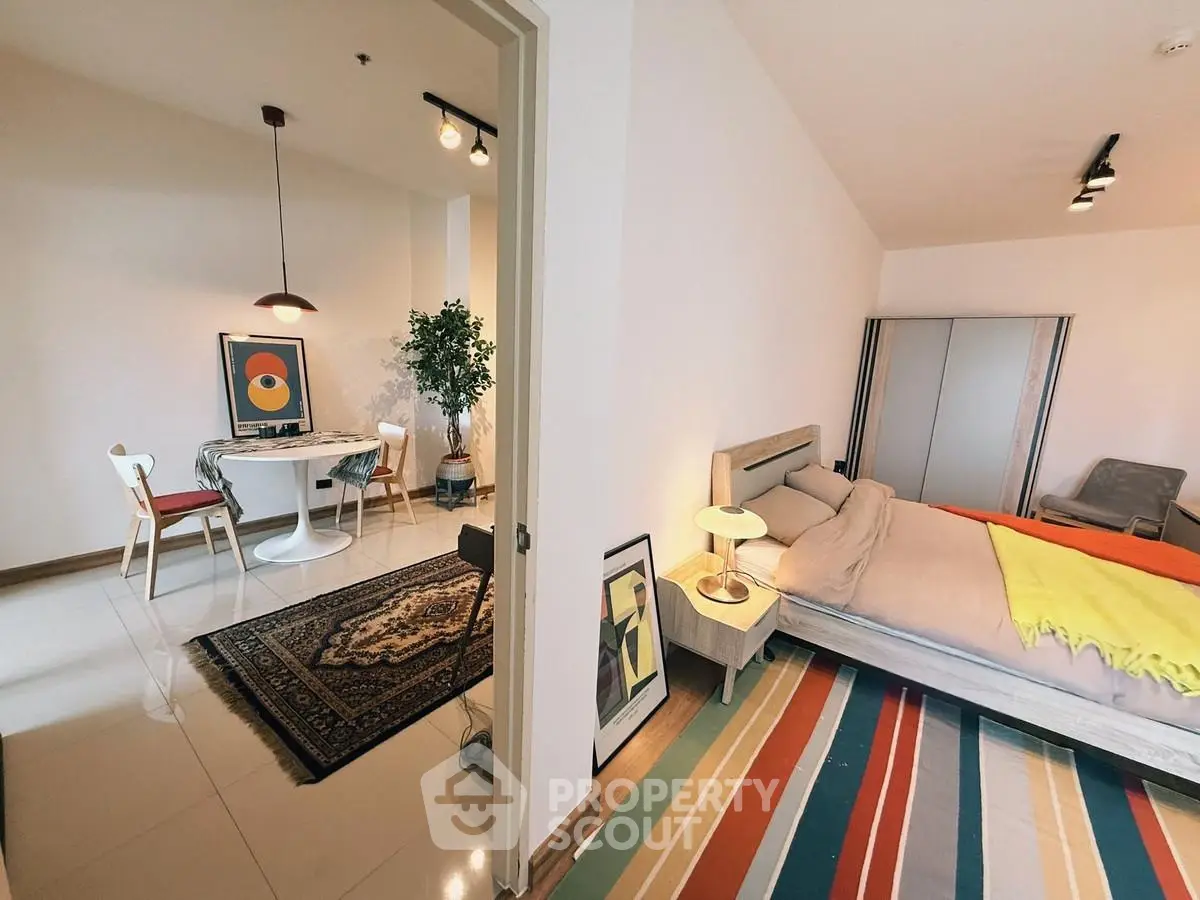 Stylish modern bedroom with colorful rug and adjacent dining area in open layout apartment.