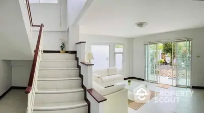 Spacious living room with elegant white staircase and direct garden access through sliding glass doors, featuring modern minimalist design.