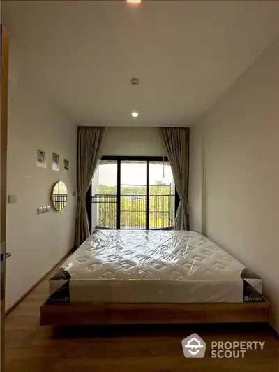 Spacious bedroom with large windows offering ample natural light and a serene view, complemented by elegant drapery and a modern wooden bed frame.