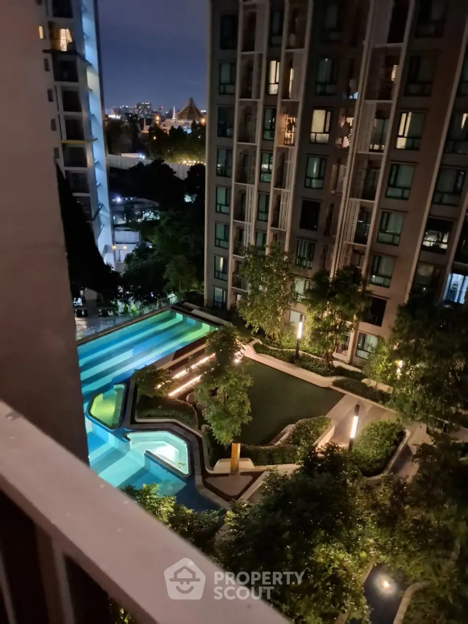 Luxurious high-rise apartment with stunning night view of illuminated pool and lush garden.