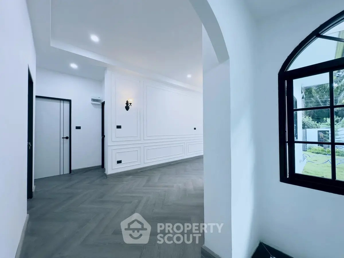 Elegant interior with herringbone flooring and classic wall paneling, featuring a large window for natural light.