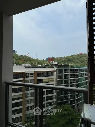 Modern apartment balcony with panoramic city view and lush greenery.