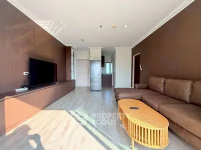 Spacious living room with modern decor and natural light, featuring a large sofa and flat-screen TV.