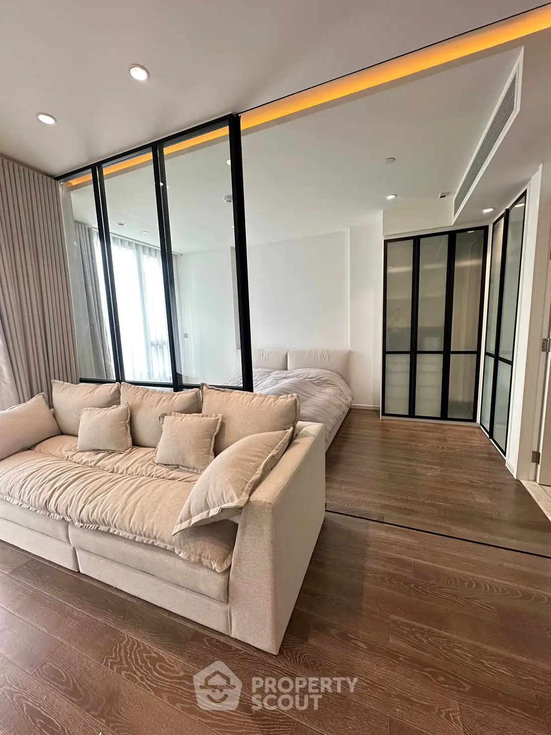 Modern open-concept living room with glass partition and cozy bedroom