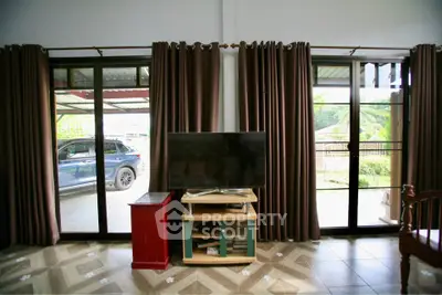 Spacious living room with large windows and outdoor view, featuring a TV and elegant curtains.