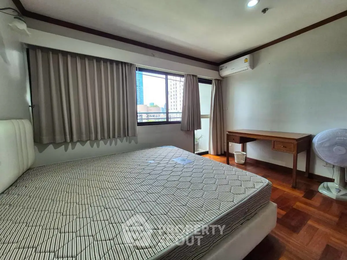 Spacious bedroom with large window and wooden flooring in modern apartment