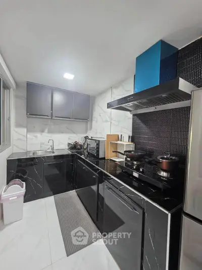 Modern kitchen with sleek black cabinetry and marble countertops, featuring stainless steel appliances and ample storage.