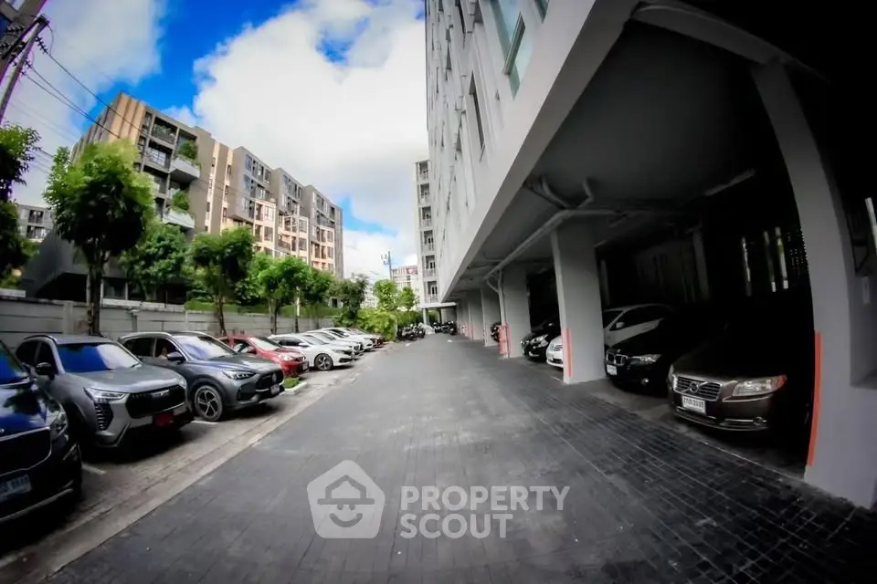 Modern apartment building with spacious parking area and multiple cars parked.