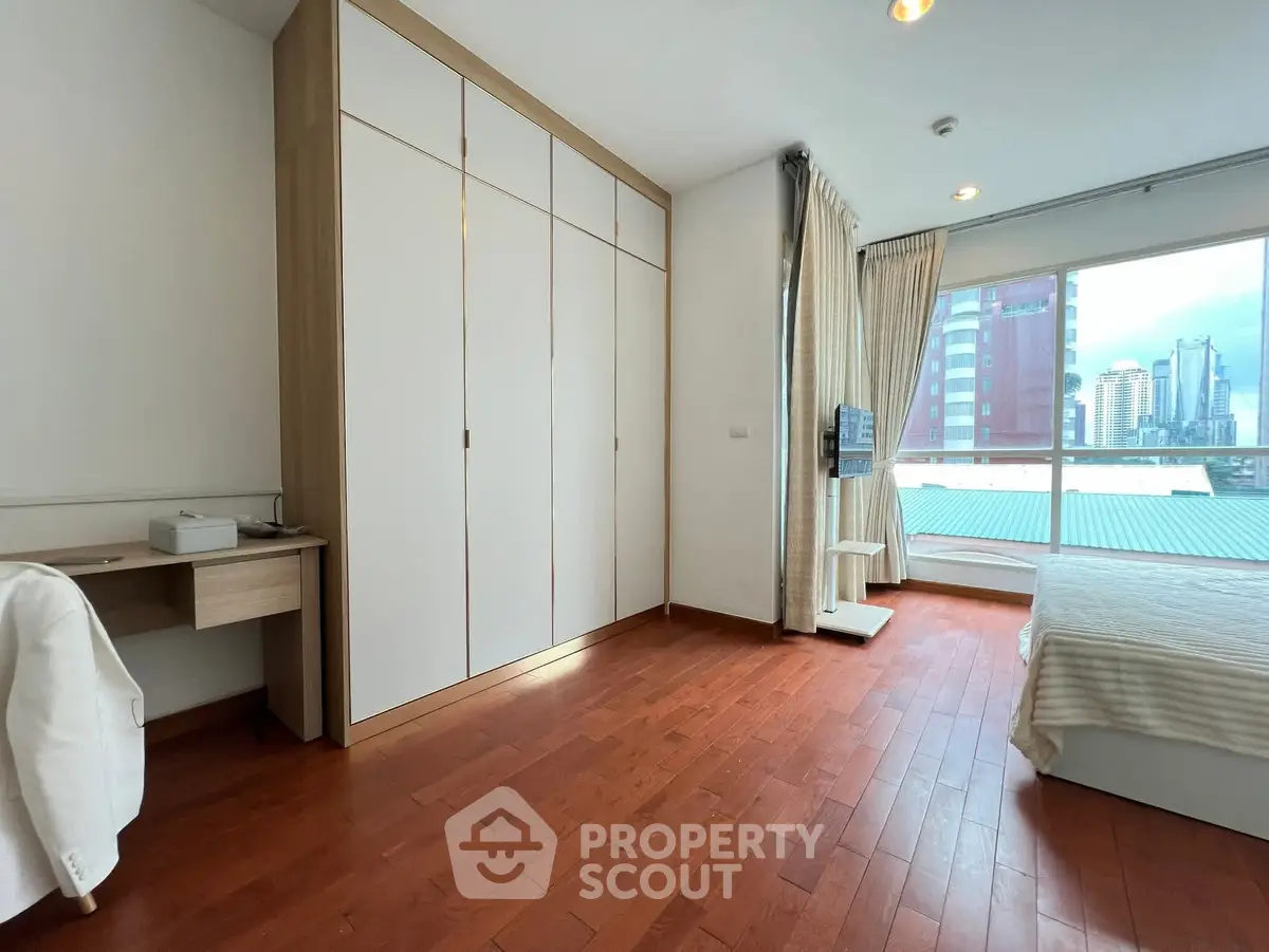 Spacious bedroom with city view, wooden flooring, and ample closet space.