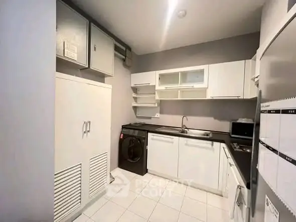 Modern kitchen with sleek white cabinets and built-in appliances, featuring a washing machine and ample storage.