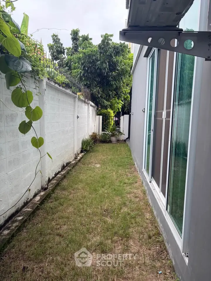 Charming side garden with lush greenery and modern glass facade, perfect for relaxation and outdoor enjoyment.