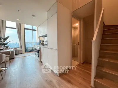 Modern open-plan living area with kitchen and city view, featuring sleek design and natural light.