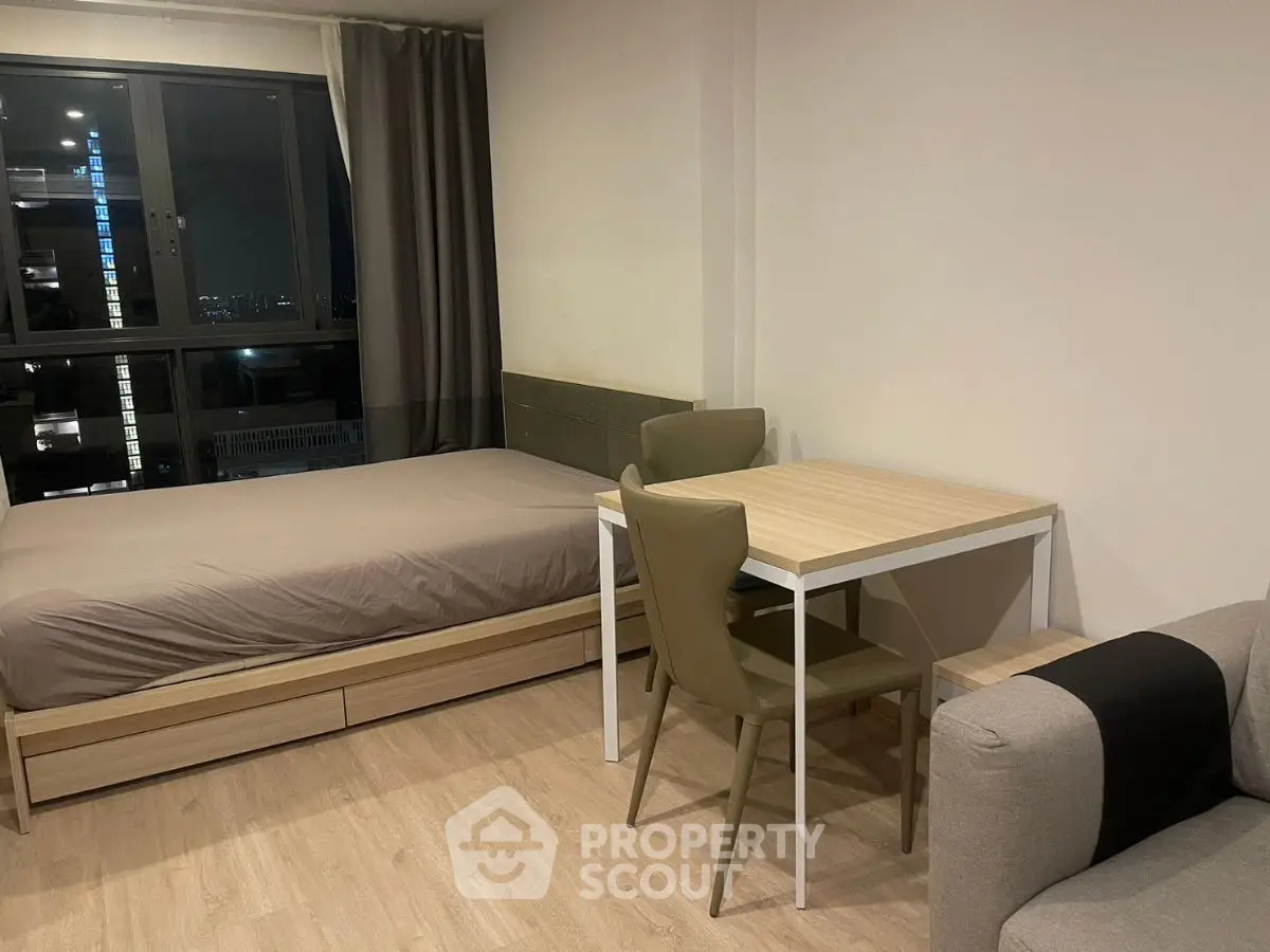 Modern studio apartment with bed, dining table, and city view window.