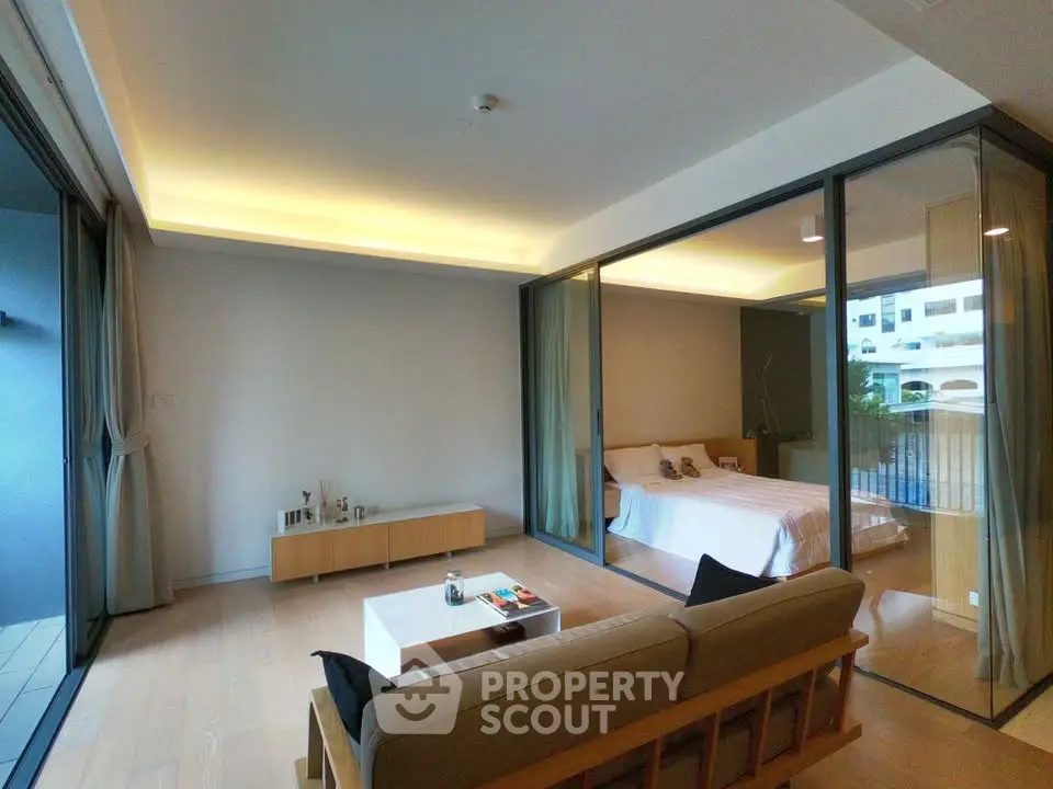 Modern living room with glass-walled bedroom and sleek furniture in a stylish apartment.